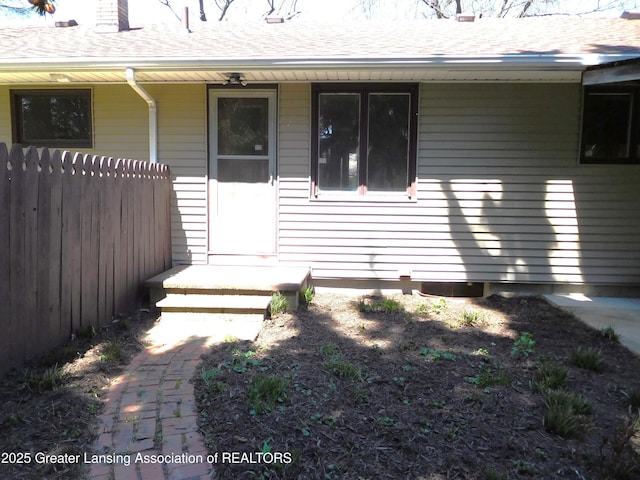 view of exterior entry featuring roof with shingles and fence