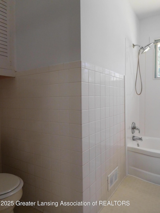 bathroom with tile walls, washtub / shower combination, visible vents, and toilet