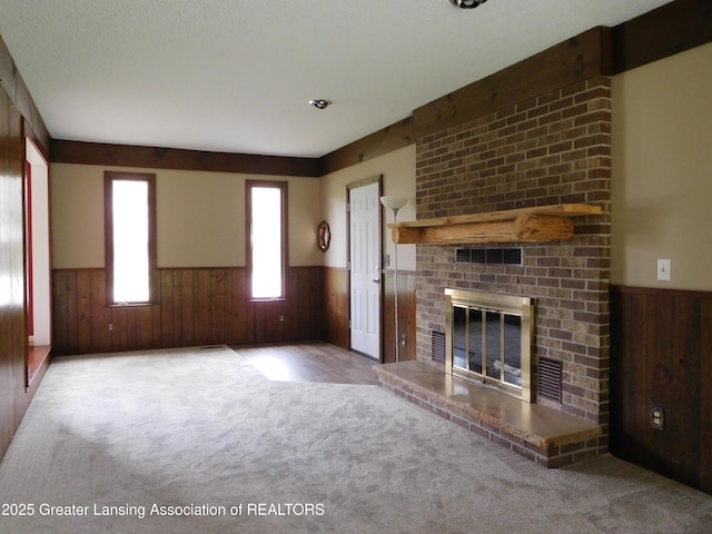unfurnished living room featuring wainscoting, a fireplace, wood walls, and carpet flooring