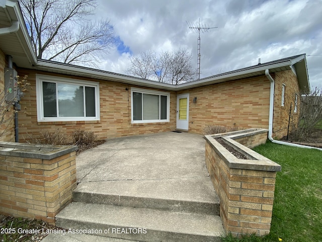 view of exterior entry with a patio and brick siding