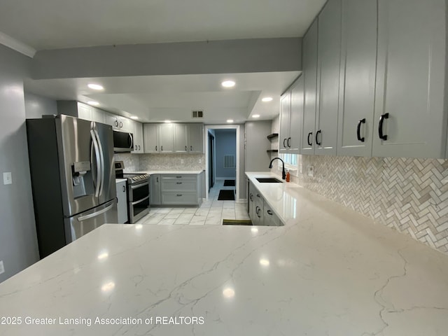 kitchen with a sink, tasteful backsplash, visible vents, light stone counters, and appliances with stainless steel finishes