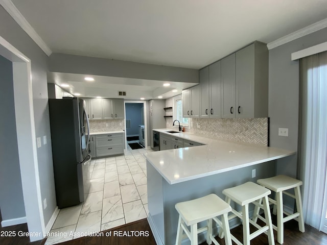 kitchen featuring decorative backsplash, marble finish floor, a sink, stainless steel refrigerator with ice dispenser, and a peninsula