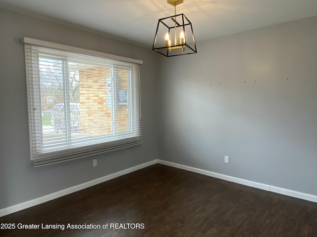 spare room with plenty of natural light, a notable chandelier, dark wood-style floors, and baseboards
