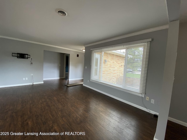 empty room with baseboards, visible vents, dark wood-style floors, and crown molding