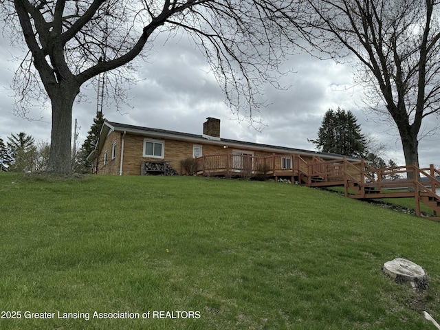 back of house featuring a chimney, a yard, a deck, and brick siding