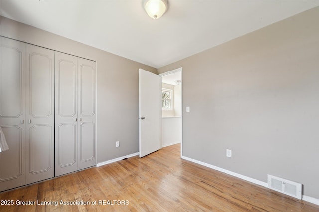 unfurnished bedroom featuring visible vents, baseboards, light wood finished floors, and a closet