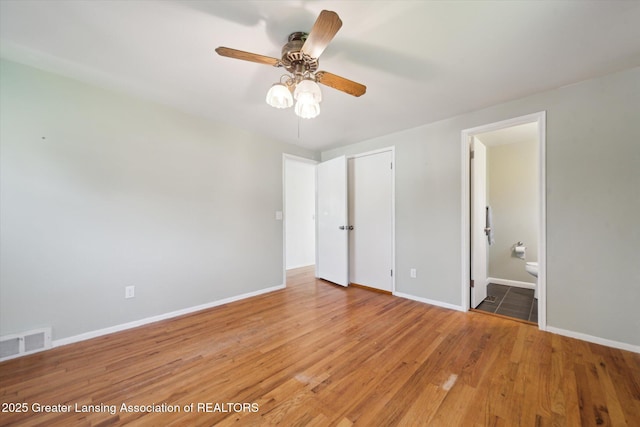 unfurnished bedroom with visible vents, wood finished floors, baseboards, ensuite bathroom, and a ceiling fan