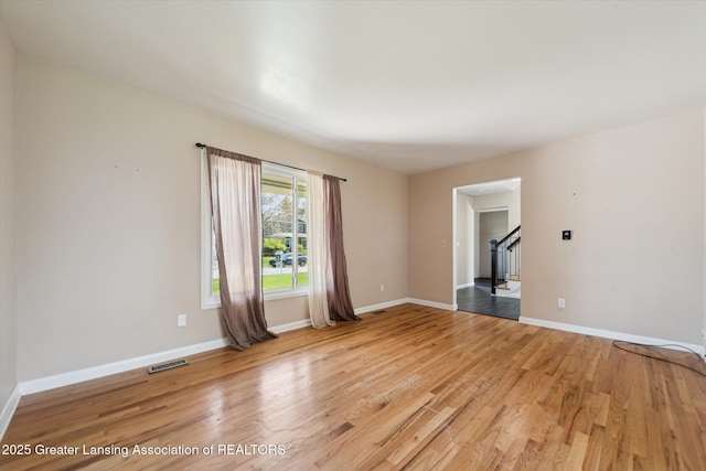 empty room featuring visible vents, stairs, light wood-style flooring, and baseboards