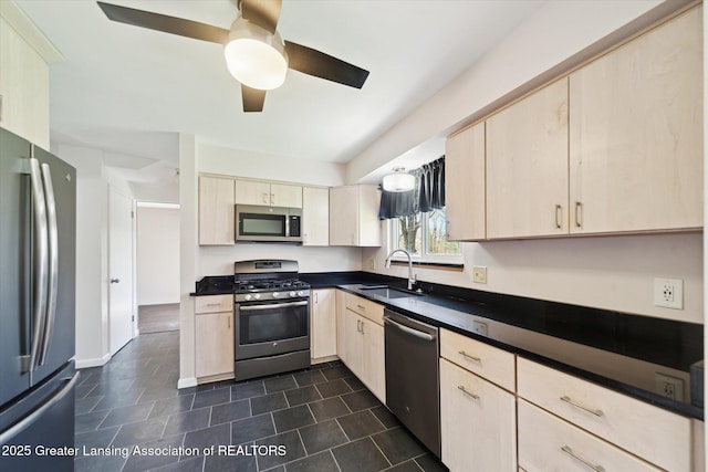 kitchen with light brown cabinetry, dark countertops, ceiling fan, a sink, and stainless steel appliances