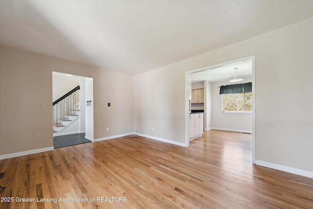spare room featuring stairway, baseboards, and light wood finished floors
