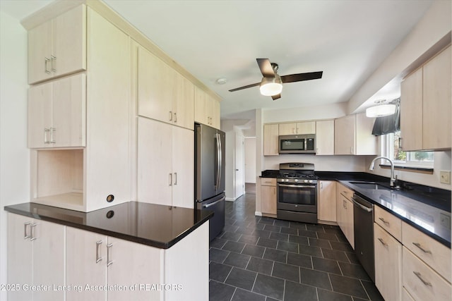 kitchen featuring light brown cabinetry, dark countertops, appliances with stainless steel finishes, and a sink