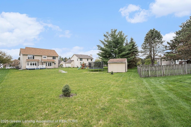 view of yard featuring a trampoline, fence, an outdoor structure, a playground, and a shed