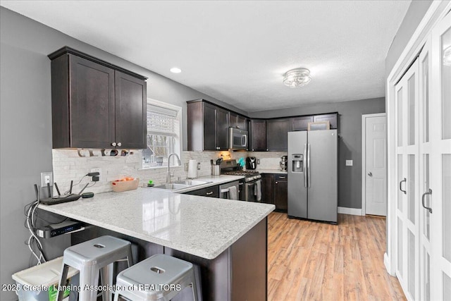 kitchen with dark brown cabinets, a sink, decorative backsplash, a peninsula, and appliances with stainless steel finishes