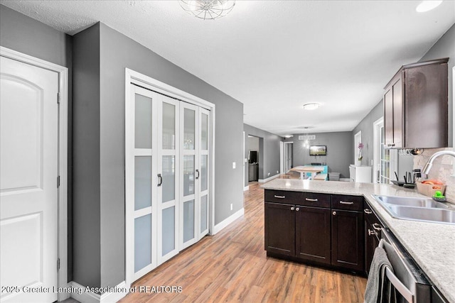 kitchen featuring a sink, light wood-style floors, dishwasher, light countertops, and a peninsula