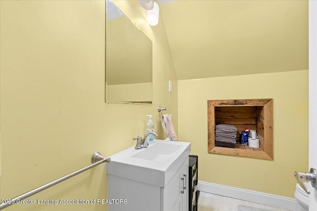 bathroom featuring baseboards, lofted ceiling, and vanity