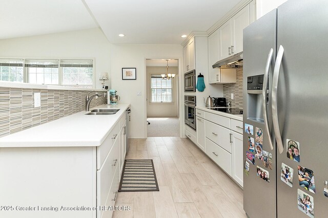 kitchen with a sink, stainless steel appliances, backsplash, a wealth of natural light, and under cabinet range hood