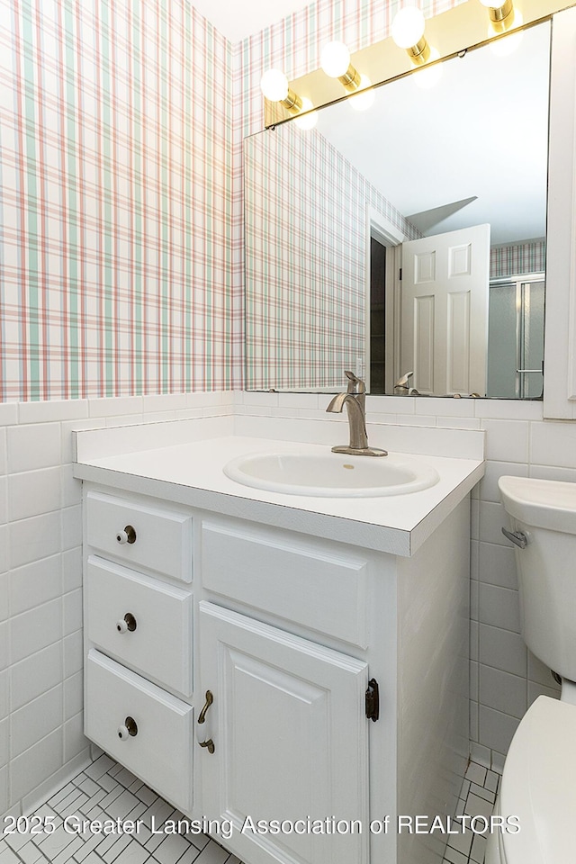 bathroom with vanity, tile walls, toilet, and wallpapered walls
