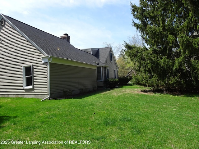 view of side of property with a yard, a chimney, and roof with shingles