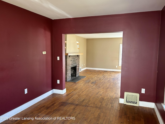1909 W Holmes Rd, Lansing, MI 48910 - unfurnished living room with baseboards, hardwood / wood-style flooring, visible vents, and a brick fireplace