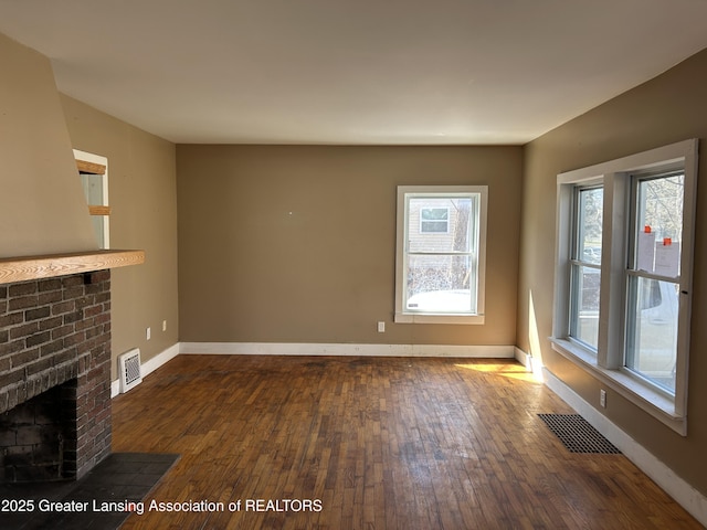 1909 W Holmes Rd, Lansing, MI 48910 - unfurnished living room featuring baseboards, a brick fireplace, dark wood-type flooring, and visible vents