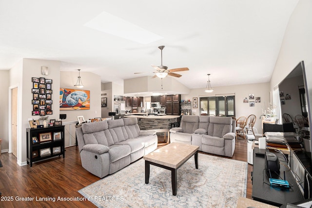 living room featuring dark wood finished floors, baseboards, ceiling fan, and vaulted ceiling with skylight