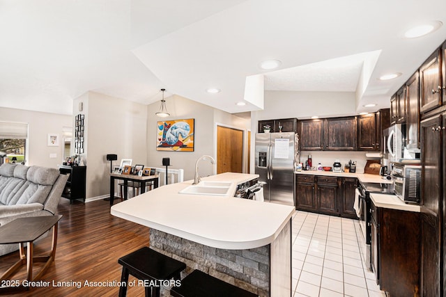 kitchen with a sink, stainless steel appliances, light countertops, dark brown cabinets, and an island with sink