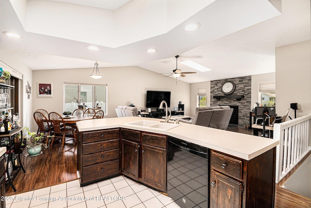 kitchen featuring a sink, dark brown cabinets, black dishwasher, a ceiling fan, and a stone fireplace
