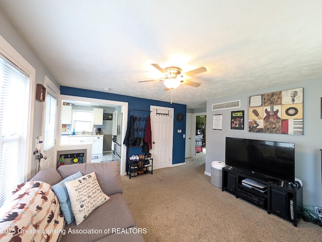 living room featuring ceiling fan, light carpet, and a textured ceiling
