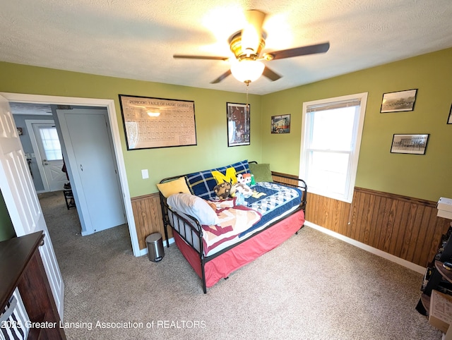 carpeted bedroom with wooden walls, multiple windows, and wainscoting