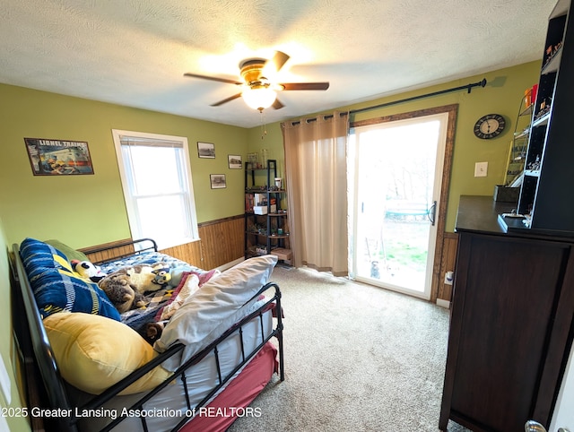 bedroom featuring wood walls, a wainscoted wall, access to exterior, and a textured ceiling