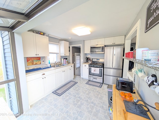 kitchen featuring appliances with stainless steel finishes, a sink, white cabinetry, and light countertops