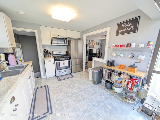 kitchen with a sink, light floors, white cabinetry, light countertops, and appliances with stainless steel finishes