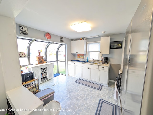 kitchen with light countertops, freestanding refrigerator, a sink, and white cabinetry