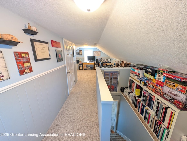hall featuring vaulted ceiling, a textured ceiling, an upstairs landing, and carpet floors