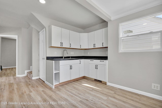 1435 New York Ave, Lansing, MI 48906 - kitchen with dark countertops, baseboards, light wood-type flooring, white cabinets, and a sink