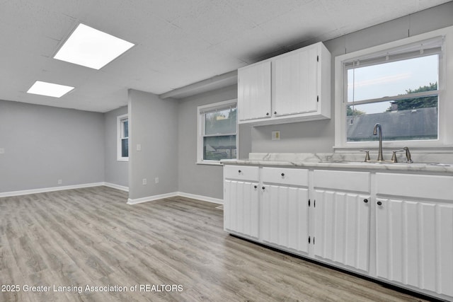 425 Filley St, Lansing, MI 48906 - kitchen with a sink, light countertops, white cabinets, light wood-type flooring, and baseboards
