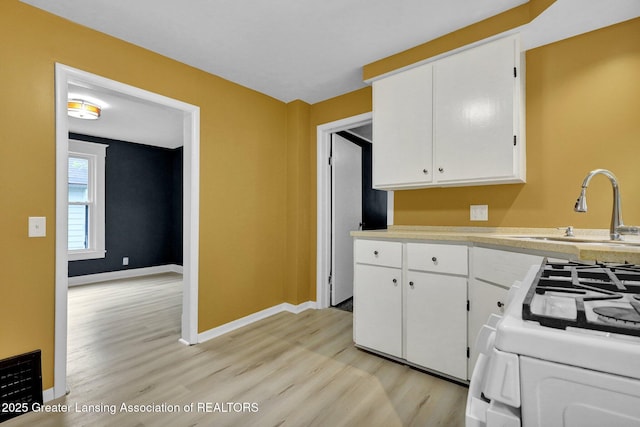 908 Larned St, Lansing, MI 48912 - kitchen featuring light wood finished floors, white gas range, white cabinetry, a sink, and light countertops