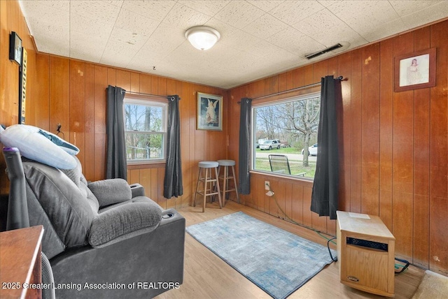 living area with wooden walls, light wood-style floors, and visible vents