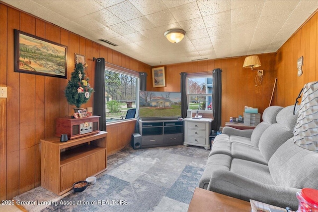 carpeted living area featuring wooden walls, a healthy amount of sunlight, and visible vents