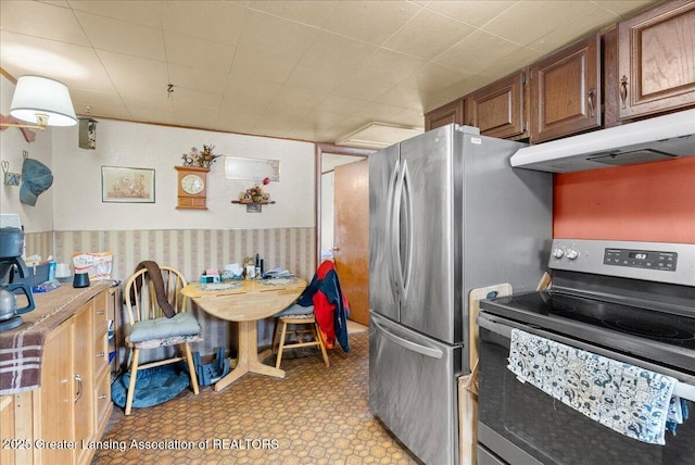 kitchen featuring wallpapered walls, under cabinet range hood, light floors, brown cabinetry, and appliances with stainless steel finishes