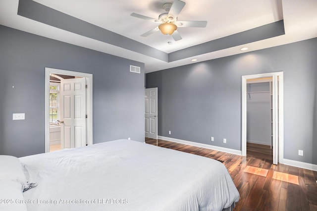 12714 Ospreys Way, Dewitt, MI 48820 - bedroom featuring wood finished floors, a walk in closet, baseboards, visible vents, and a tray ceiling