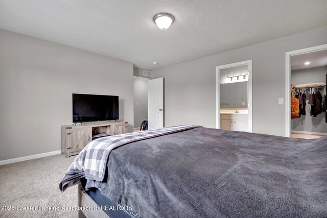 12001 Bryde Dr, Rives Junction, MI 49277 - carpeted bedroom featuring visible vents, baseboards, ensuite bathroom, a walk in closet, and a sink