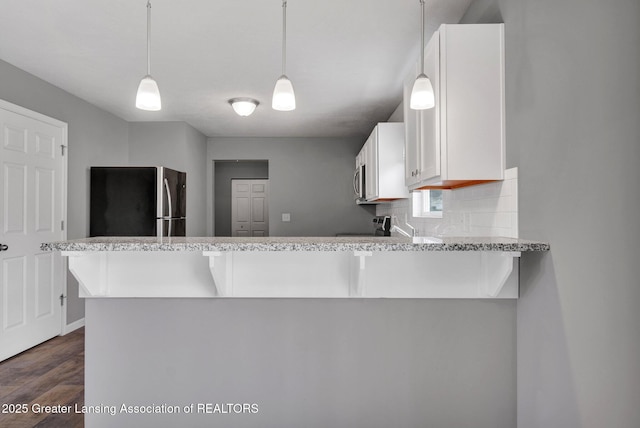 12001 Bryde Dr, Rives Junction, MI 49277 - kitchen featuring appliances with stainless steel finishes, a peninsula, white cabinetry, dark wood-type flooring, and backsplash