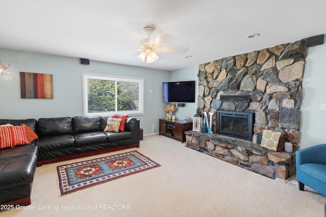carpeted living area featuring ceiling fan and a stone fireplace