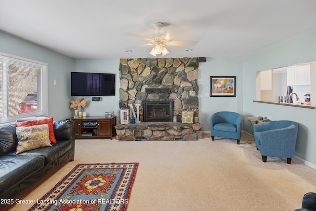 carpeted living area featuring a sink, a ceiling fan, a stone fireplace, and baseboards