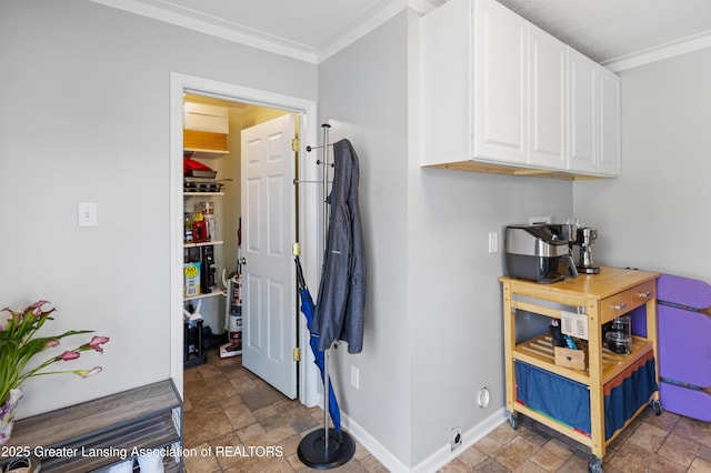 interior space featuring baseboards, cabinet space, stone finish floor, and crown molding