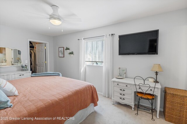 bedroom featuring a walk in closet, ceiling fan, light carpet, and baseboards