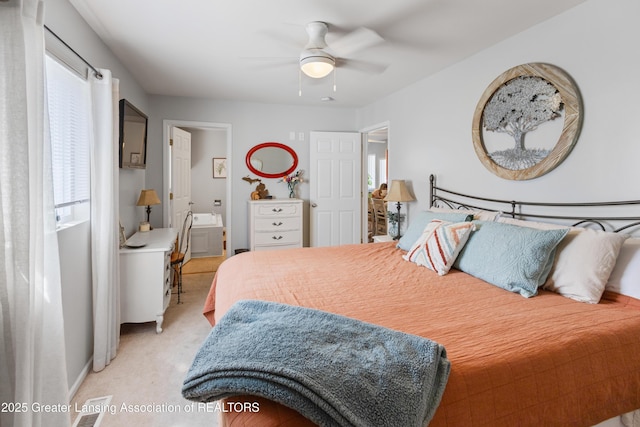 bedroom featuring light colored carpet, a ceiling fan, ensuite bath, and multiple windows