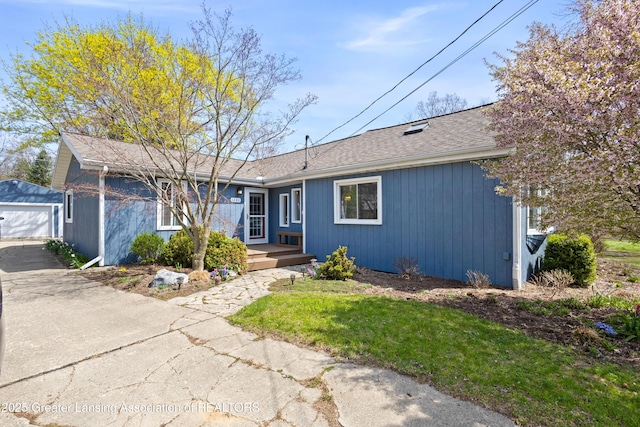 ranch-style home with an outbuilding, a detached garage, driveway, and a shingled roof
