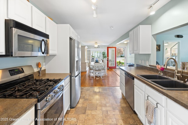 kitchen with rail lighting, dark countertops, stainless steel appliances, and a sink